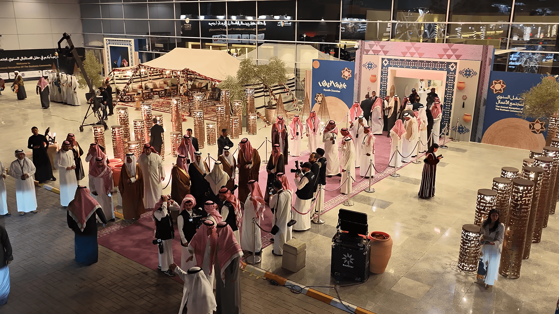 تجمع لرجال بالزي السعودي في حفل استقبال بغرفة الرياض يضم أعمدة مزخرفة وسجاداً أرجوانياً.